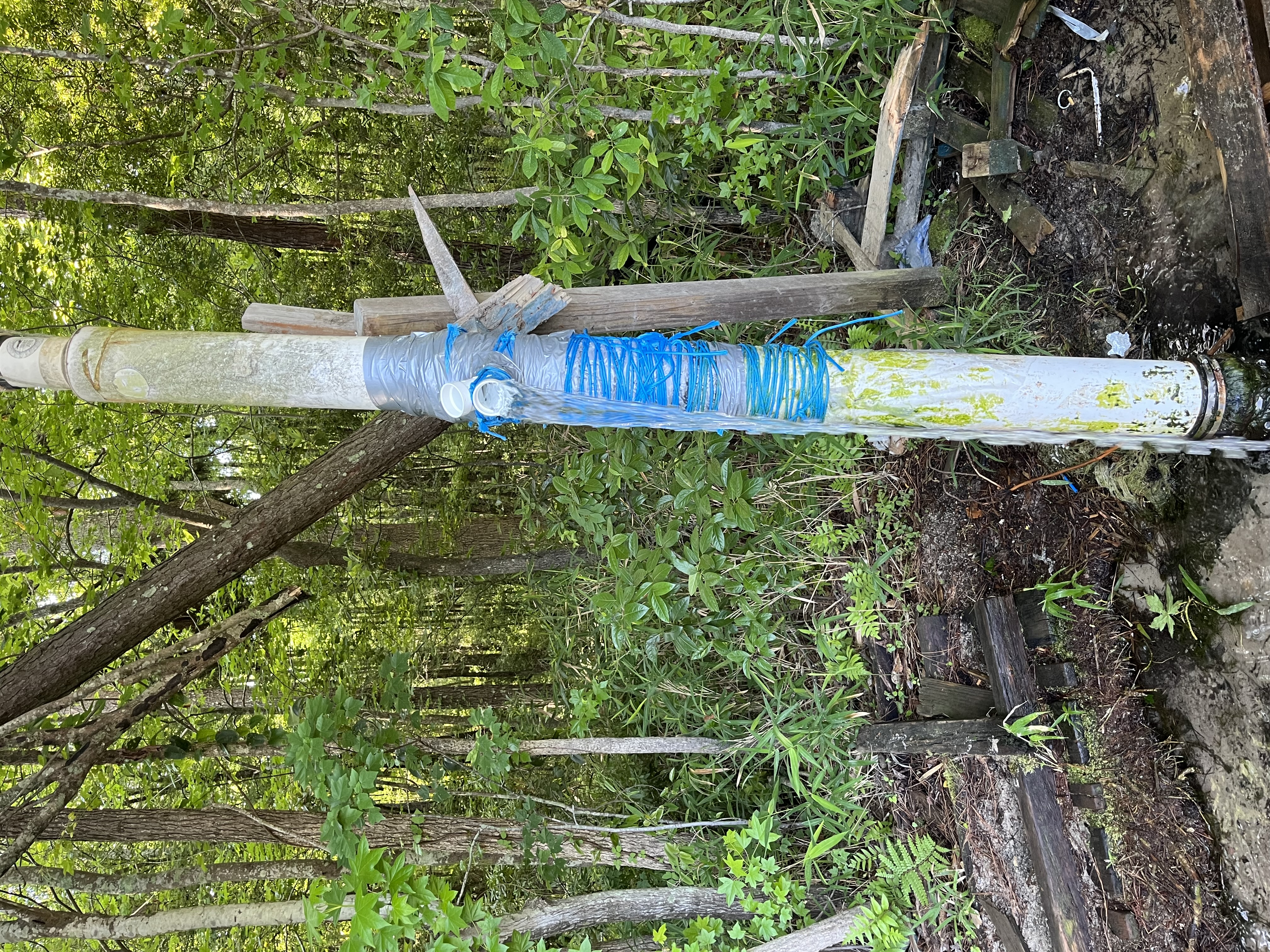 An image of a tall white PVC pipe with bright blue tape around it and water flowing out of an opening
