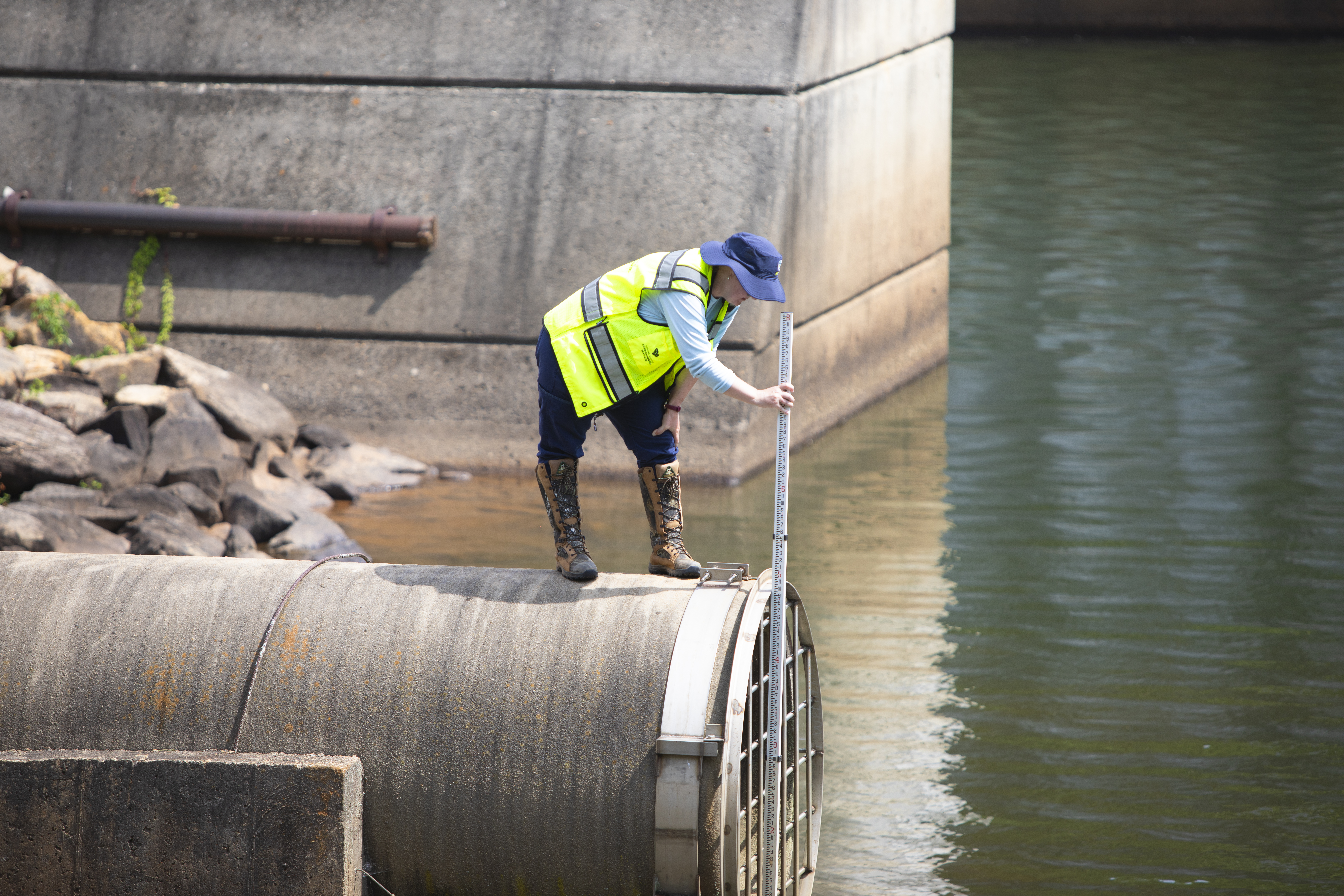 A worker in a high-visibility vest and helmet measures water levels at a dam.