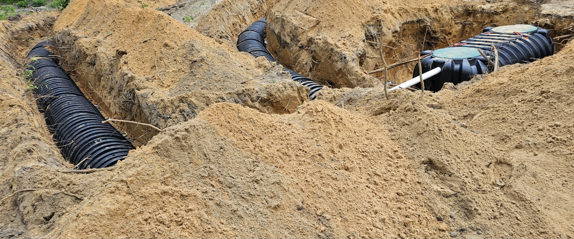 Black septic chambers installed in deep trenches surrounded by piles of sand.
