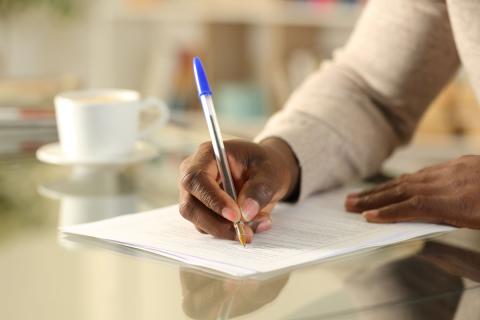 Close up of a black man hands filling out form on a desk at home